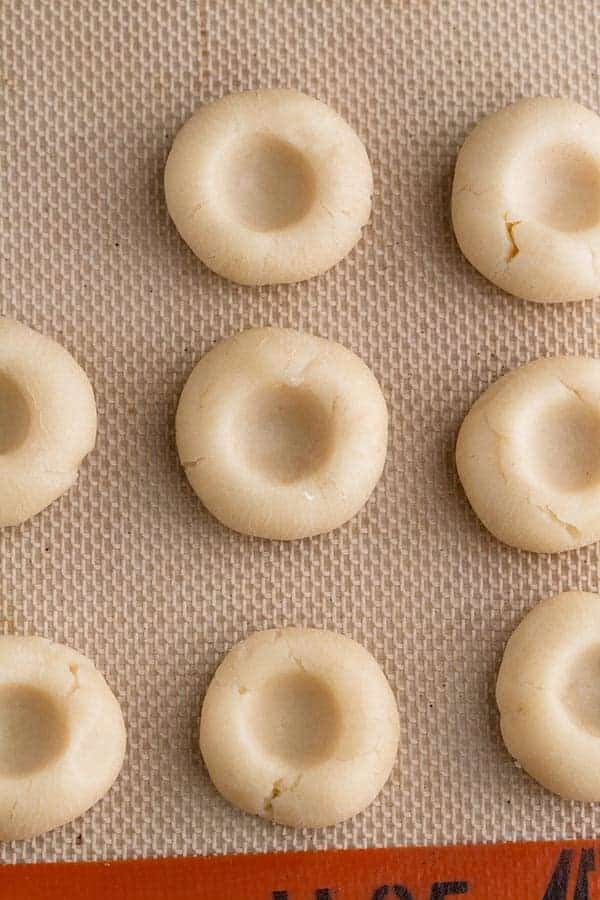 A bunch of uncooked thumbprint cookies on a silpat