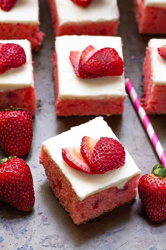 Overhead view of several squares of frosted strawberry cake with fresh strawberries on top