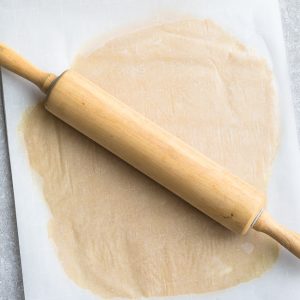 Keto Sugar Cookie dough between two pieces of parchment paper with a rolling pin