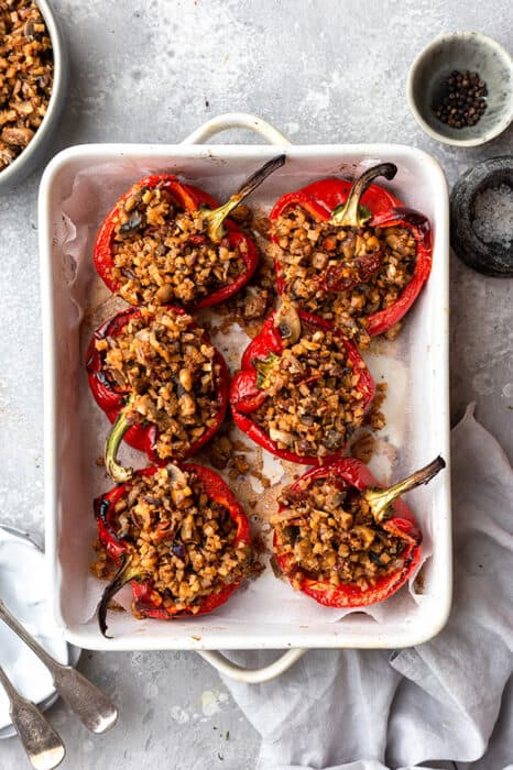 Top view of vegan stuffed peppers in a white baking dish on a grey background