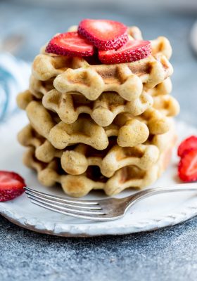 Side view of keto waffles on a white plate with strawberries and a fork