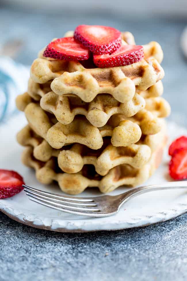 Side view of keto waffles on a white plate with strawberries and a fork