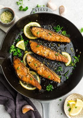 Four broiled salmon fillets in a skillet on top of a kitchen counter