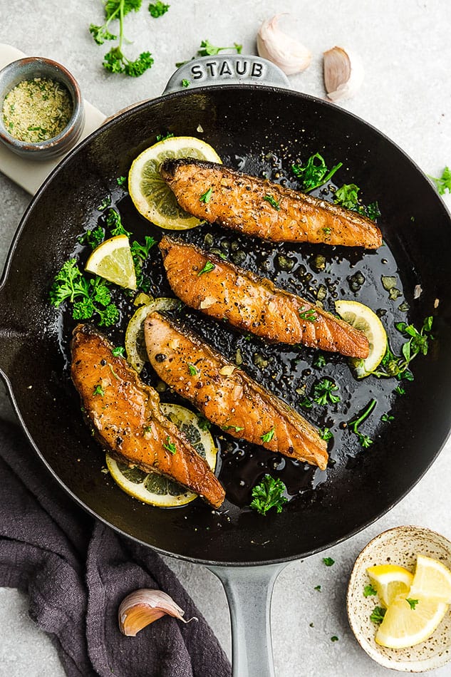 Four broiled salmon fillets in a skillet on top of a kitchen counter