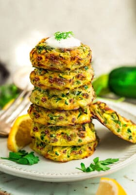 Side view of six keto zucchini fritters stacked on a white plate with lemon wedges