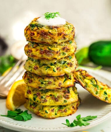 Side view of six keto zucchini fritters stacked on a white plate with lemon wedges