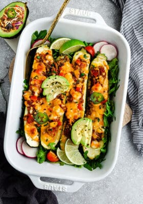 Top view of zucchini taco boats in a white casserole dish on a grey background