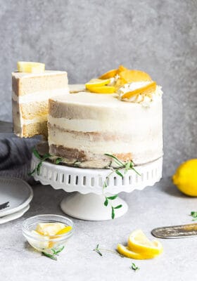 Side view of one low carb lemon cake on a white cake stand with one slice cut out