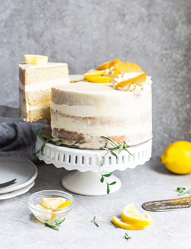 Side view of one low carb lemon cake on a white cake stand with one slice cut out