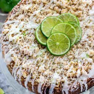 Overhead view of Key lime coffee cake with white chocolate drizzle on a clear glass plate topped with lime slices