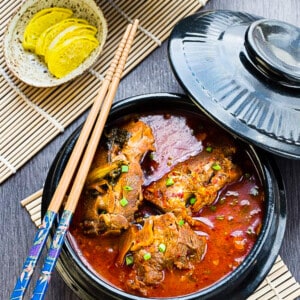 A black bowl of korean pork bone soup (Gamjatang) with chopesticks on the top on a grey background