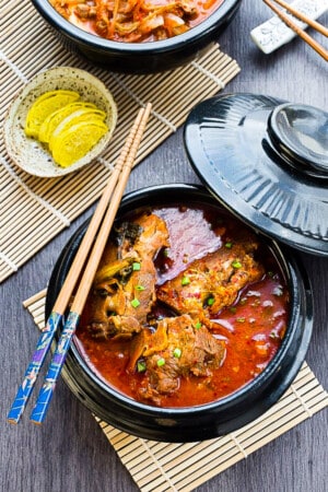 A black bowl of korean pork bone soup (Gamjatang) with chopesticks on the top on a grey background