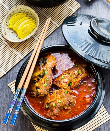 A black bowl of korean pork bone soup (Gamjatang) with chopesticks on the top on a grey background