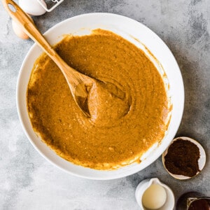 Top view of paleo pumpkin bread batter in a white bowl with a wooden spoon