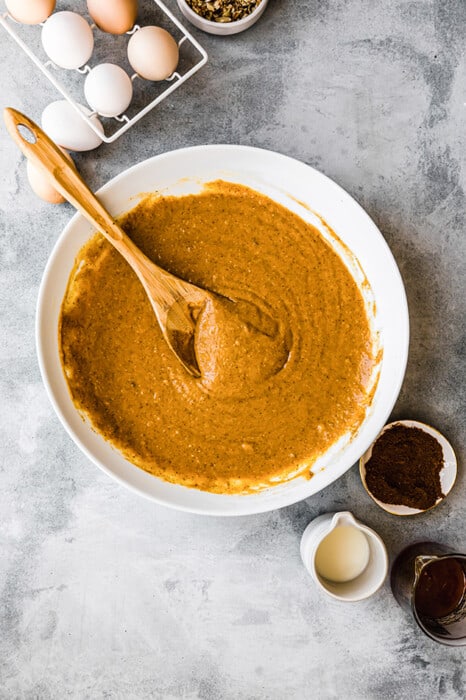 Top view of paleo pumpkin bread batter in a white bowl with a wooden spoon