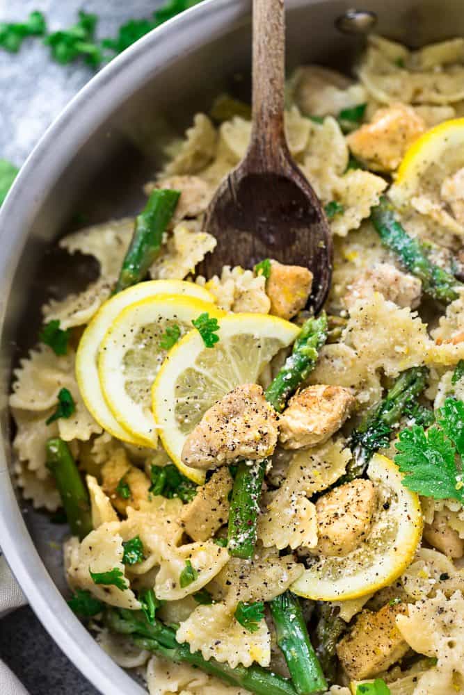 wooden spoon stirring a lemon chicken skillet dinner with fresh asparagus and lemon slices