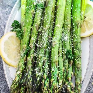 Top view of air fryer roasted asparagus on a white plate with lemon