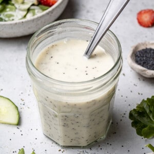 45 degree shot of creamy poppy seed dressing in a small jar with a spoon