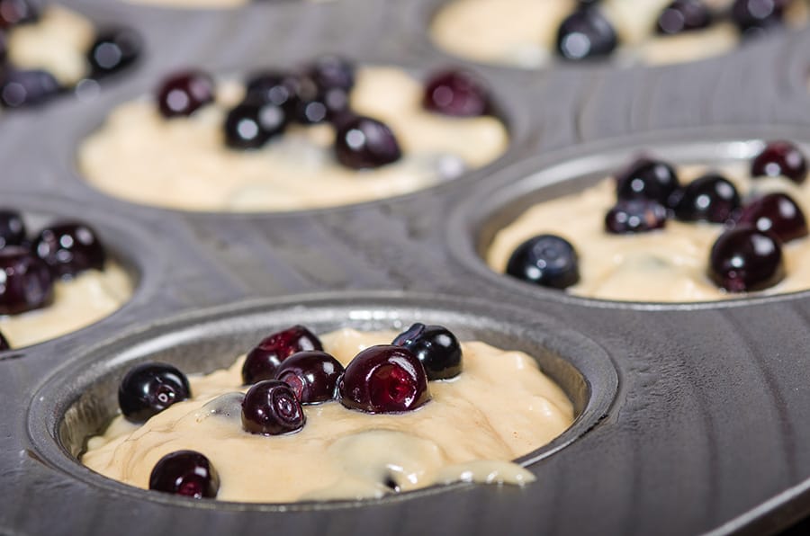 Metal muffin pan with batter and berries