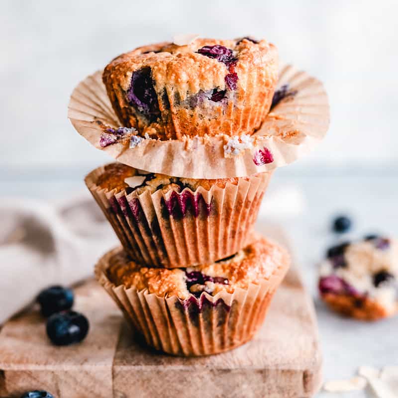 Side view of three stacked Keto Blueberry Muffins on a wooden cutting board.