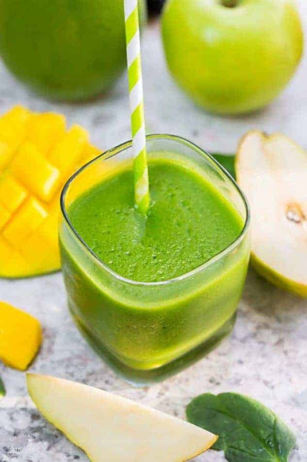 Top view of one healthy spinach smoothie in a clear glass with a straw on a grey marble background with fruit