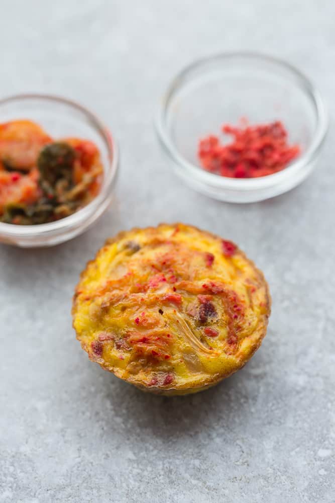 A Kimchi Egg Muffin Cup Sitting on a Gray Surface with Two Small Dishes Next to it