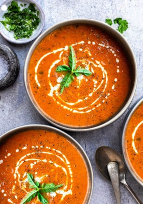 Top view of three bowls of creamy tomato soup on a grey background