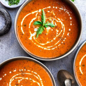 Top view of three bowls of creamy tomato soup on a grey background