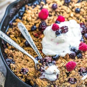 Close up view of Low carb Keto Berry Crisp with blueberries, blackberries and raspberries in a cast iron skillet with two spoons and low carb ice cream
