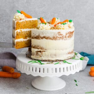 Side view of Low Carb Keto Carrot Cake on wooden cake stand with chopped pecans and carrots