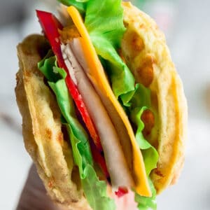 Side view of chaffle sandwich with a hand holding it up