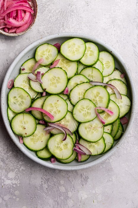 Top view of sliced cucumbers and red onions in a white bowl