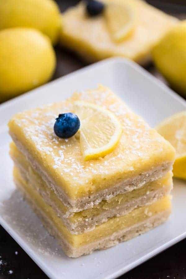 Stack of 3 Low Carb Keto Lemon Bars on a white square plate with one blueberry