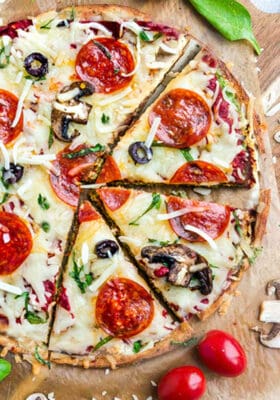 Close-up top view of low carb keto pizza crust on parchment paper with arugula, pepperoni and tomatoes