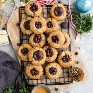 Top view of a full pile of keto peanut butter blossoms on a wire rack surrounded by tree ornaments on a grey background