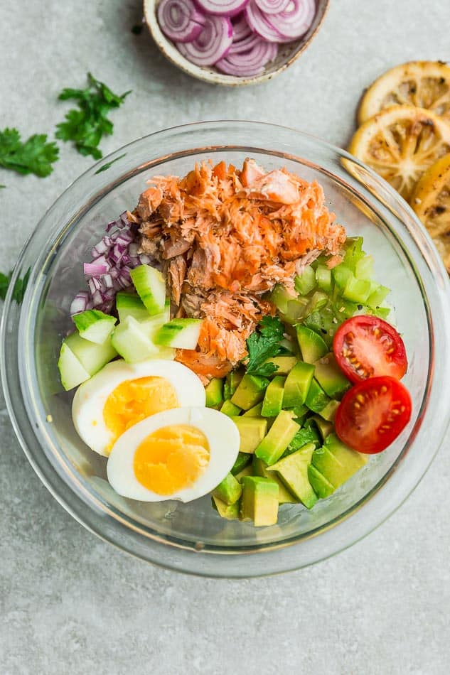 Flaked salmon in a glass mixing bowl with the prepared veggies and hard-boiled egg halves