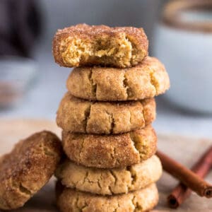 Side view of 6 stacked low carb paleo soft snickerdoodle cookies on a wire rack on a grey background with a bite