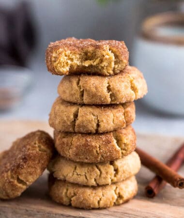Side view of 6 stacked low carb paleo soft snickerdoodle cookies on a wire rack on a grey background with a bite