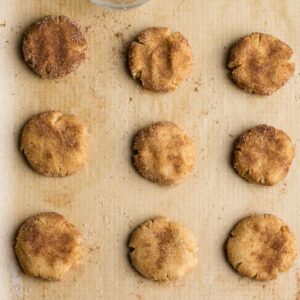Top view of 9 unbaked low carb snickerdoodle cookie dough on parchment paper on a baking sheet