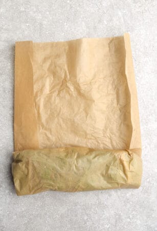 Top view of hands rolling a low carb lettuce wrap sandwich using brown parchment paper