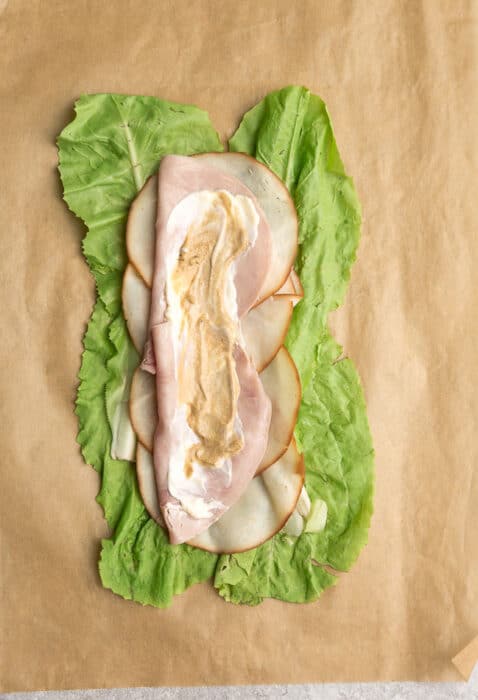 Top view of lettuce layered with turkey, ham, mustard mayonnaise on a brown parchment paper.