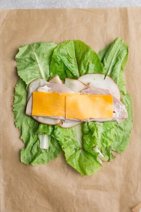 Top view of lettuce layered with turkey, ham, cheese and mayonnaise on a brown parchment paper to make keto wraps.