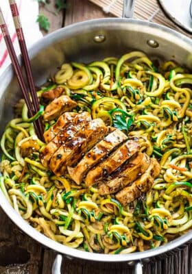 Top close-up view of Low Carb Zucchini Noodles with Chicken in a stainless steel pan on a wodden board with chopsticks
