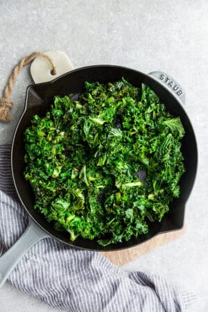 Top view of green kale in a grey cast-iron skillet on a grey background