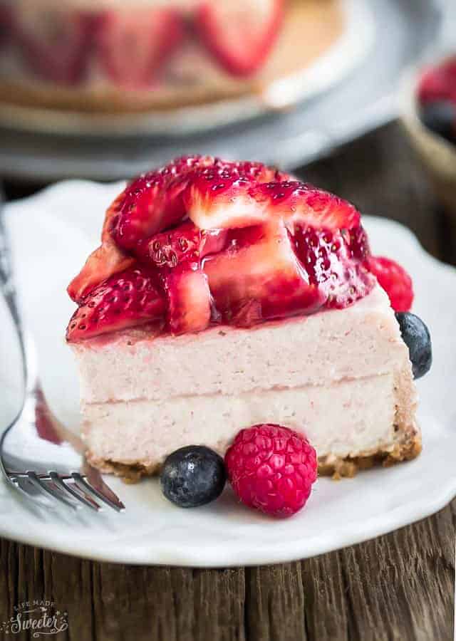 A wedge of Keto Strawberry Cheesecake on a white plate with a fork topped with fresh berries