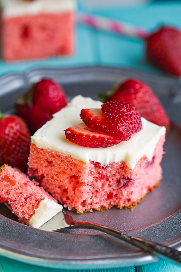 Close-up of a square of frosted strawberry cake on a plate with a bite on a fork