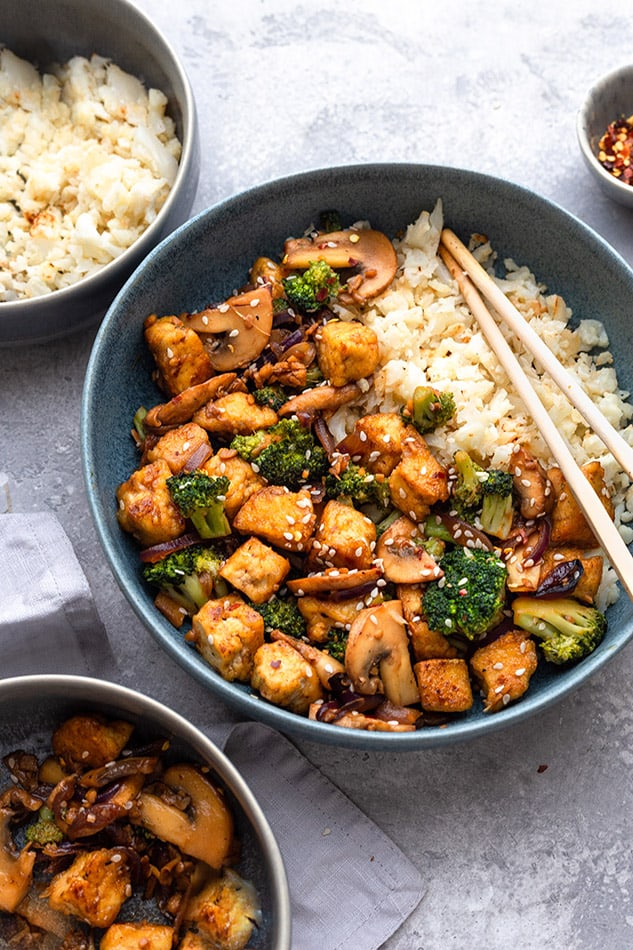 Side view of tofu stir fry in a blue bowl with chopsticks