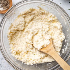 Ricotta and egg mixture in a clear mixing bowl with a wooden spoon