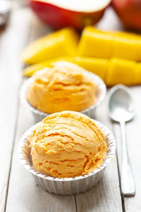 Side view of mango ice cream in a white bowl on a wooden board