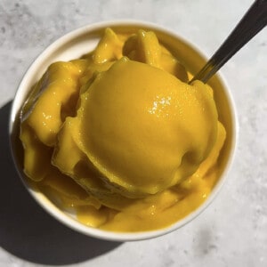 Overhead shot of a serving of mango sorbet in a white ramekin bowl with a spoon.